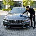 Professional detailer in black polishing the bonnet of a gleaming luxury car outdoors