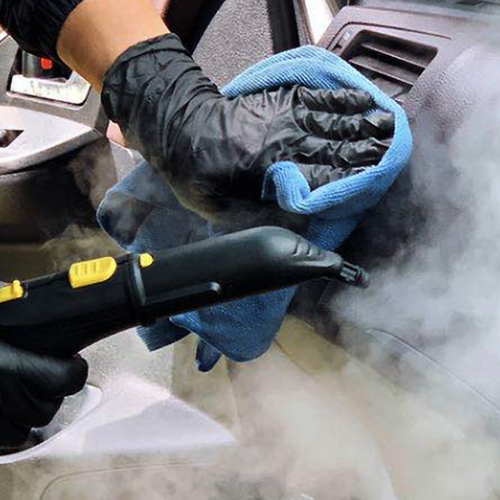 Person cleaning car interior with a steam cleaner and microfiber cloth.